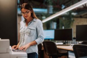 A young professional woman stands next to an office MFP