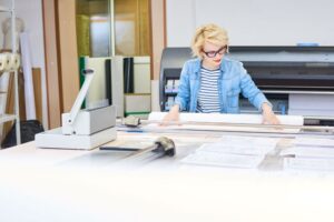 A woman working behind a wide format printer.