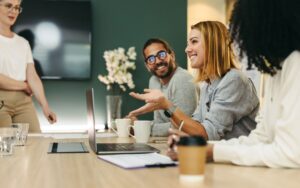 Happy office workers sit around a conference room table drinking coffee and talking while reviewing their copier lease.