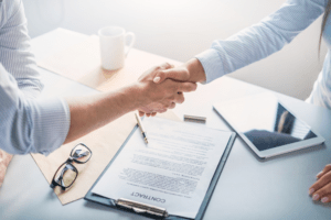 Two business professionals shaking hands over a contract on a desk, with a tablet and glasses nearby. This image symbolizes a successful agreement, often seen in office printer rental services, emphasizing trust and partnership in business transactions.