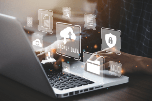 A person working on a laptop with various virtual icons related to data backup, security, and cloud storage, representing the importance of Managed IT Services. The floating icons illustrate key IT services such as data protection, file management, and cybersecurity.