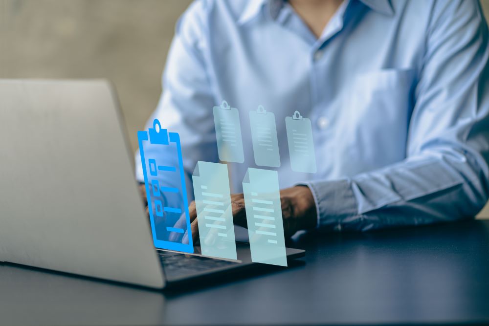 Close up of an employee behind a laptop with icons of files and clip boards next to it, signifying business document management tools.